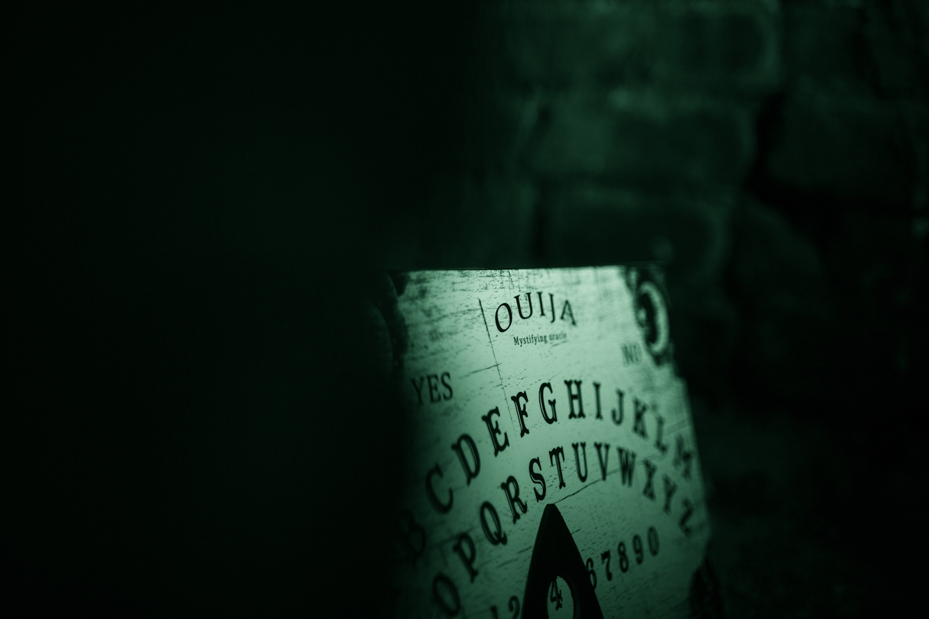 Photograph of a ouija board in a dark brick alcove. The image is toned green as a result of being made under infrared light.