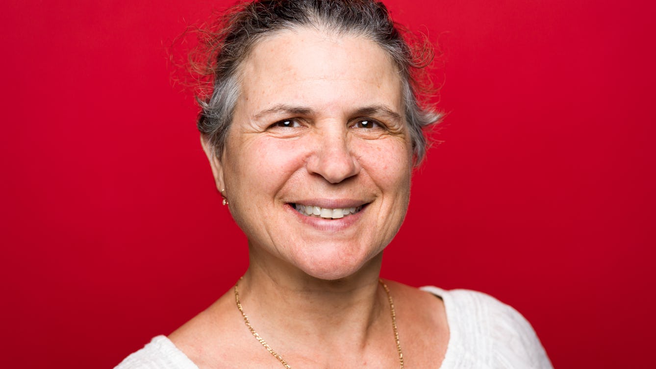 Head and shoulders photographic portrait of Golda Dahan on a red background.