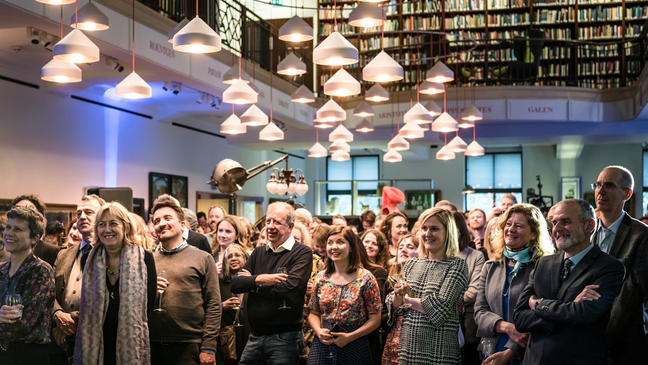 Photograph of an audience standing in the Reading Room at Wellcome Collection listening to a performance.