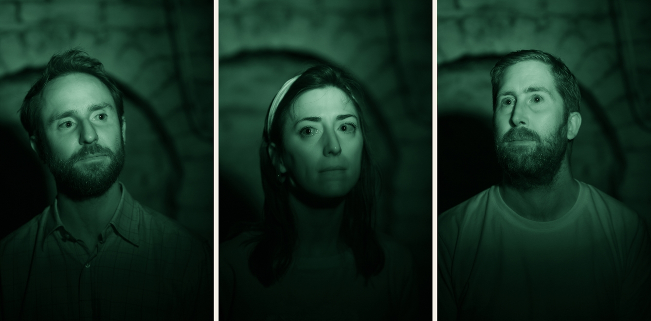 Photograph triptych of the head and shoulders of three people. Behind them is the brickwork arch in a cellar. The image is toned green as a result of being made under infrared light.