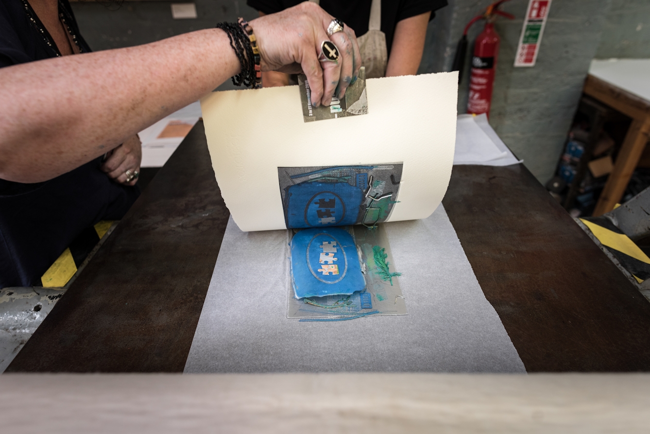 Photograph of a woman's hand lifting up some art paper to reveal a newly pressed print.