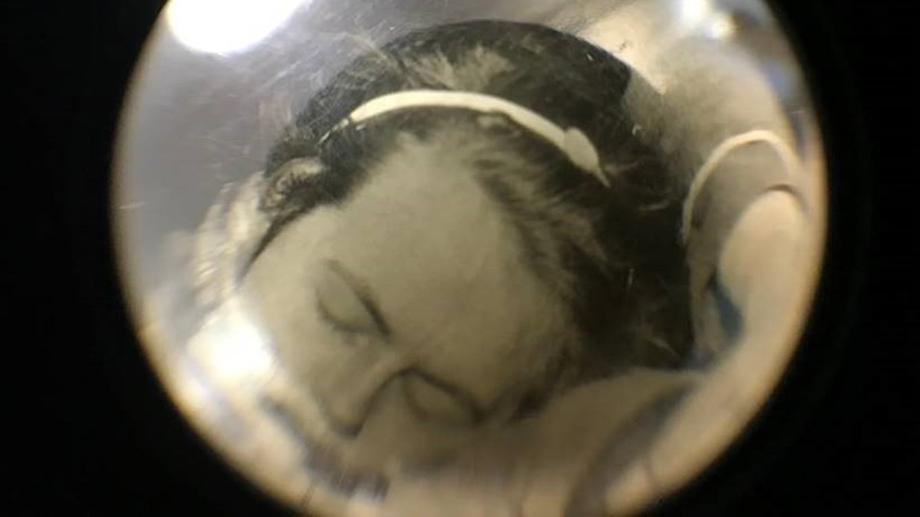 Photograph of a vintage photographic print showing a woman's head, distorted through a glass sphere.