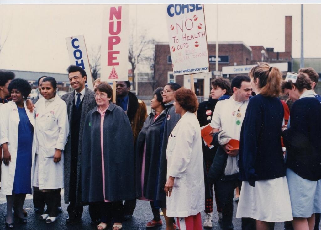 Colour photograph of people gathered at a strike. Many wear nurses' uniforms or white coats. Placards held include "COHSE", "NUPE" and "COHSE. No to health. cuts Save your health service."