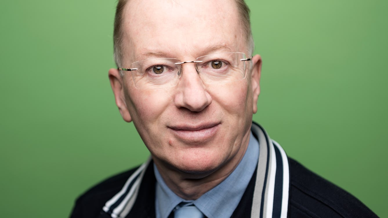 Photographic portrait of John Wilson against a green background.
