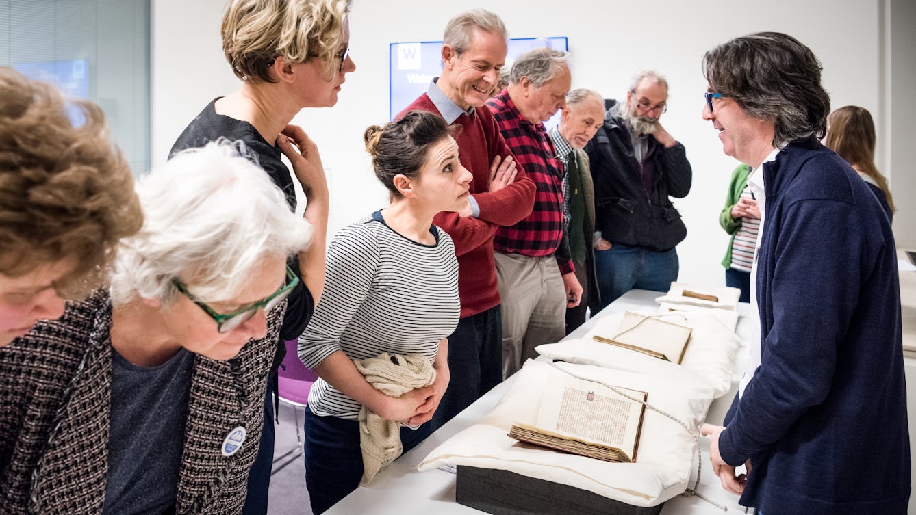 Photograph showing visitors examining archive material displayed on a table whilst talking to library staff.
