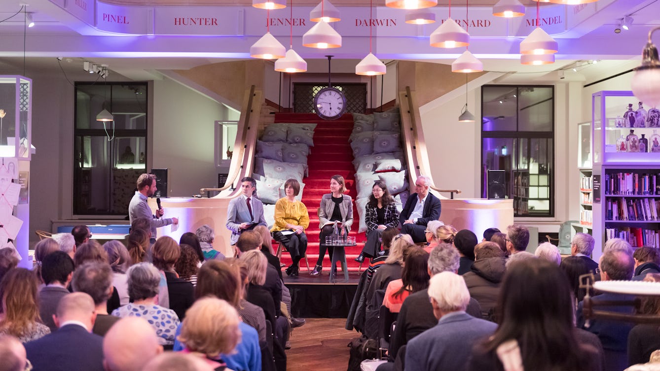 Photograph of a panel sitting on a stage, in conversation. They're in the Reading Room at Wellcome Collection. In front of them is an audience.