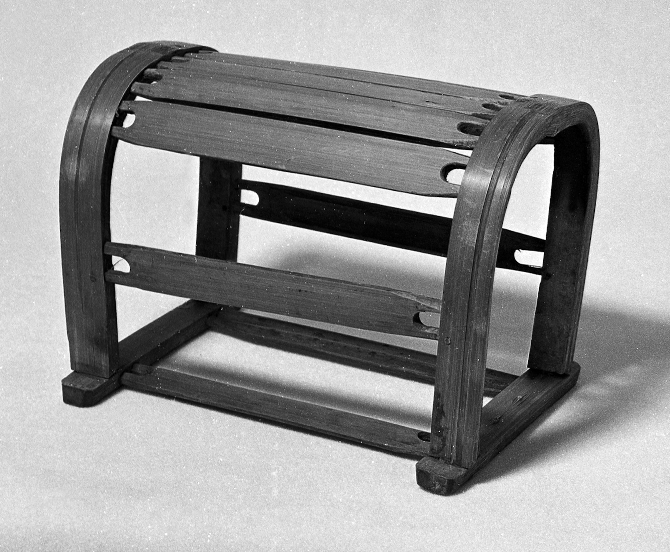 Black and white photograph of a wooden pillow, which looks like half a barrel with some of the wood missing.