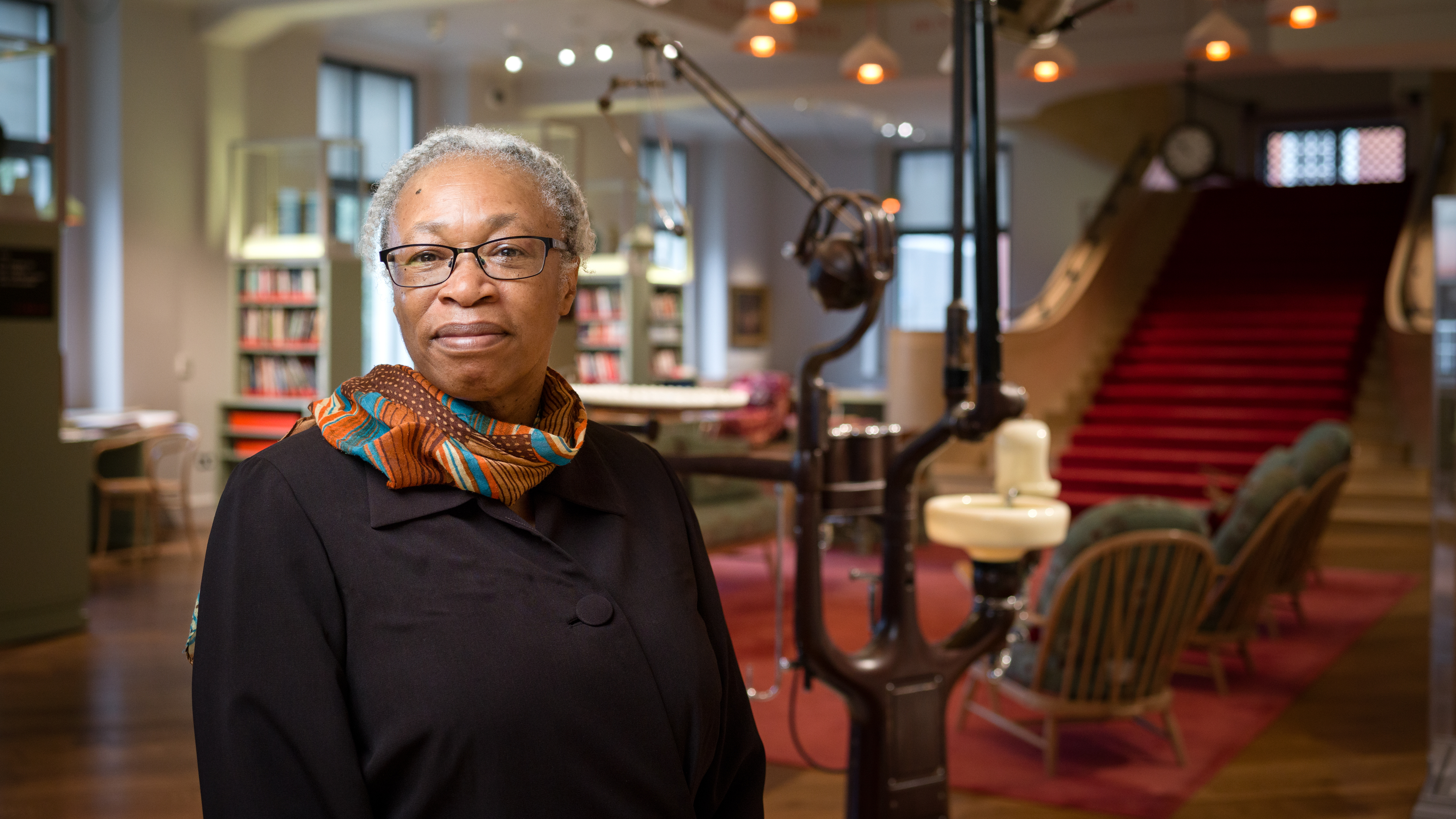 Photographic head and shoulders portrait of artist Joy Gregory standing in the Reading Room at Wellcome Collection.