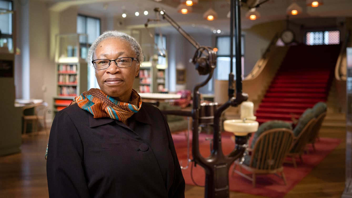 Photographic head and shoulders portrait of artist Joy Gregory standing in the Reading Room at Wellcome Collection.