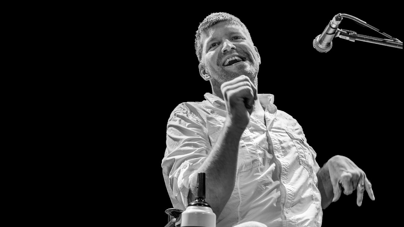 Photograph in black and white of a man giving a performance into a microphone.