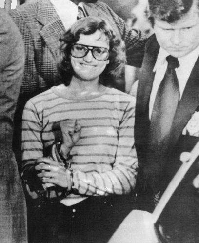A young woman in handcuffs grins and holds a clenched fist
