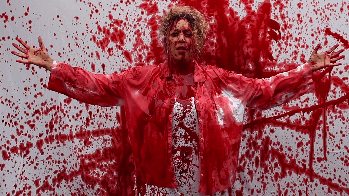 Salena Godden standing against a backdrop splattered with red paint