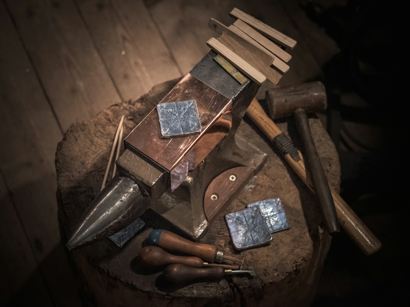 Photograph of a lead plate resting on an anvil.  Surrounding the lead, to the right, are the tools with which the impressions are made, including specially crafted wooden sticks and a wooden mallet.