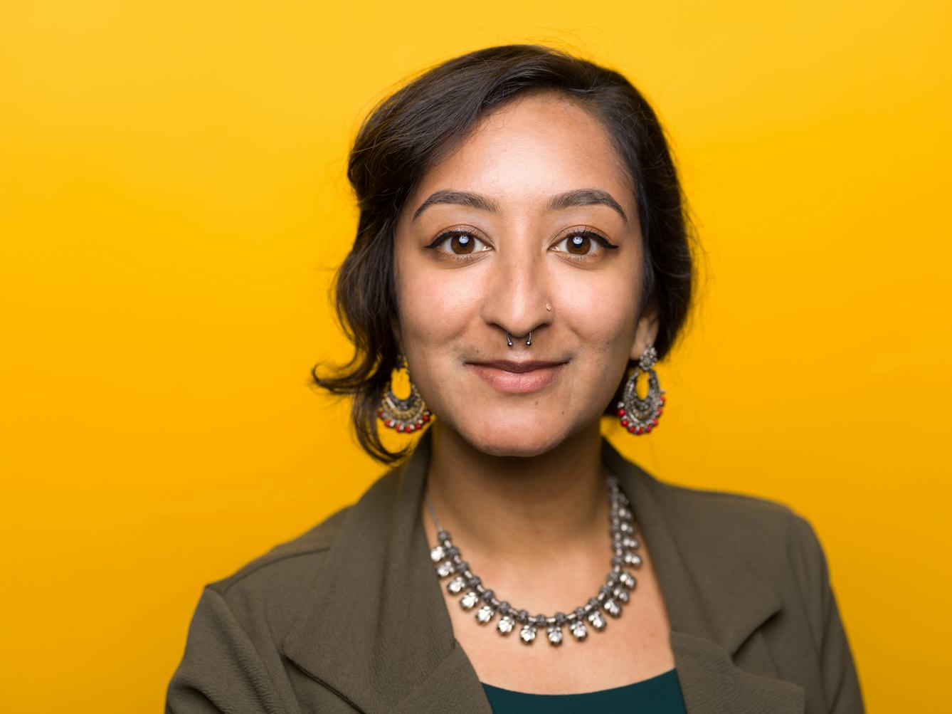 Close-up photographic portrait of Shelley Angelie Saggar's face and shoulders, against a yellow background.