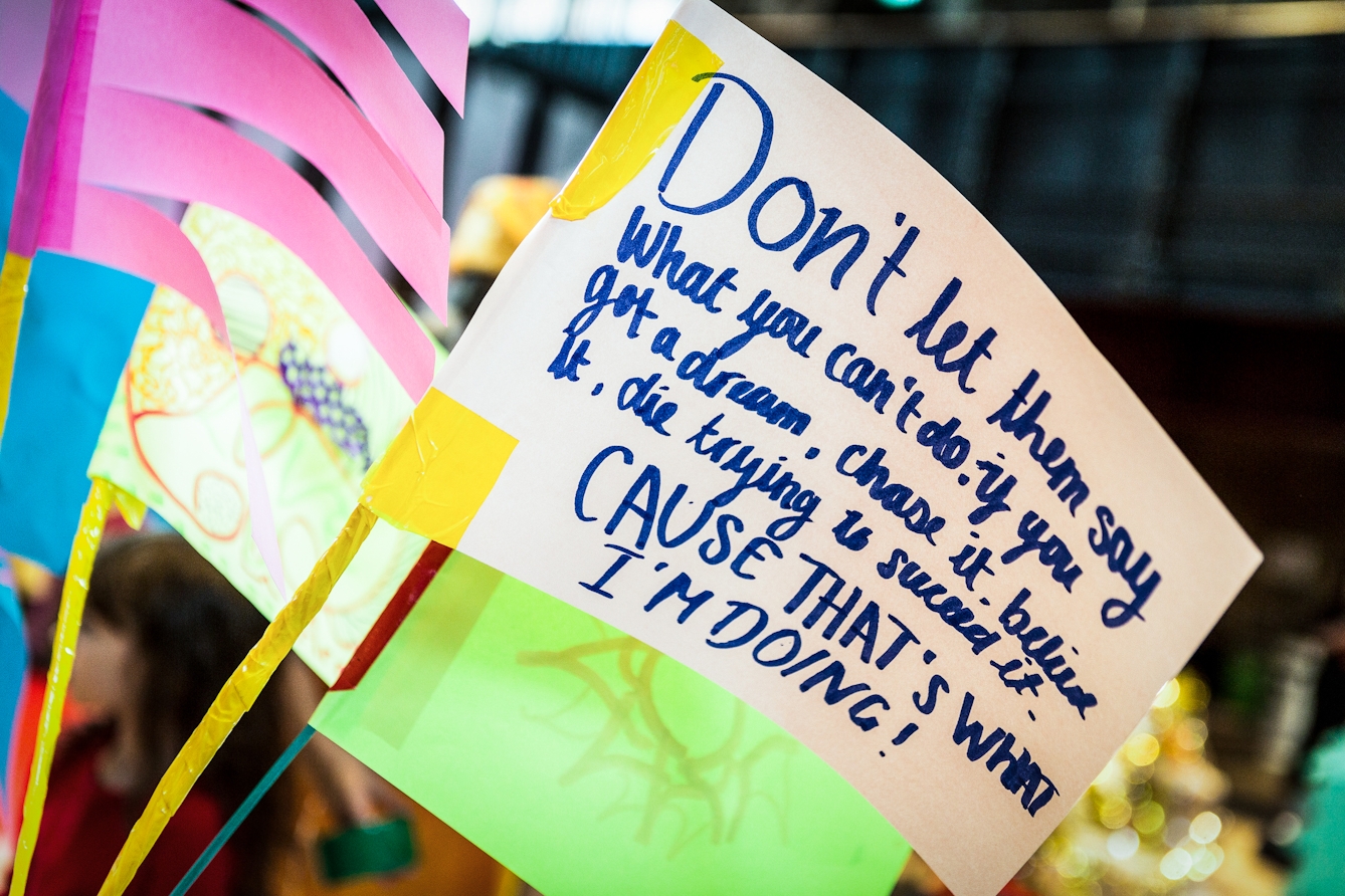 Photograph at an event showing a close up of a hand made flag on which is written, 'Don't let them say what you can't do. If you got a dream, chase it, believe it, die trying to succeed it. Cause that's what I'm doing!'.