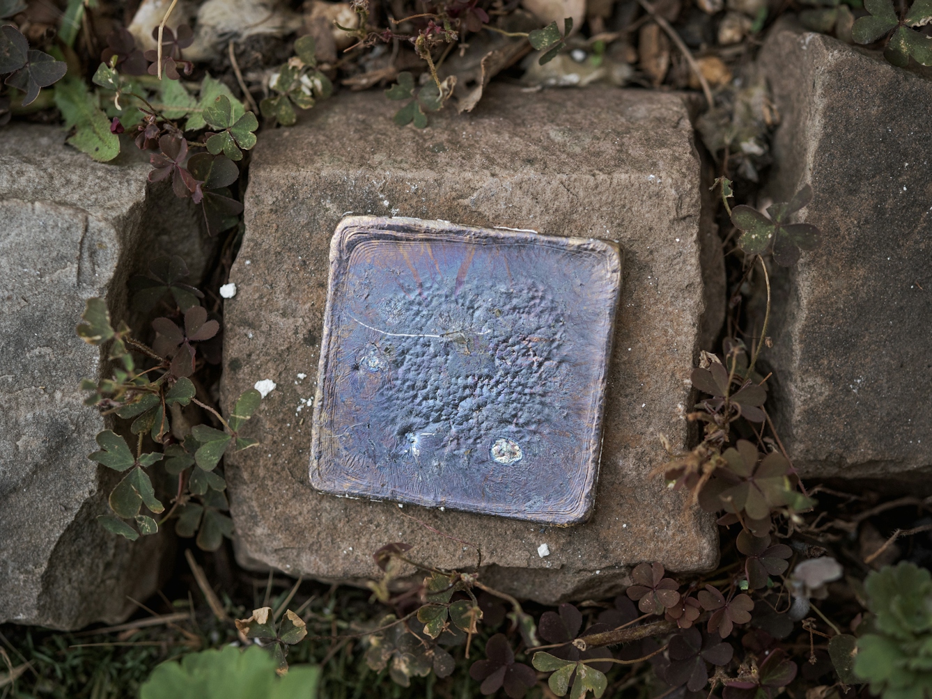 Photograph of a lead plate cooling on a stone.  The lead shows signs of lead oxide on the surface, giving off blue and purple colouring.
