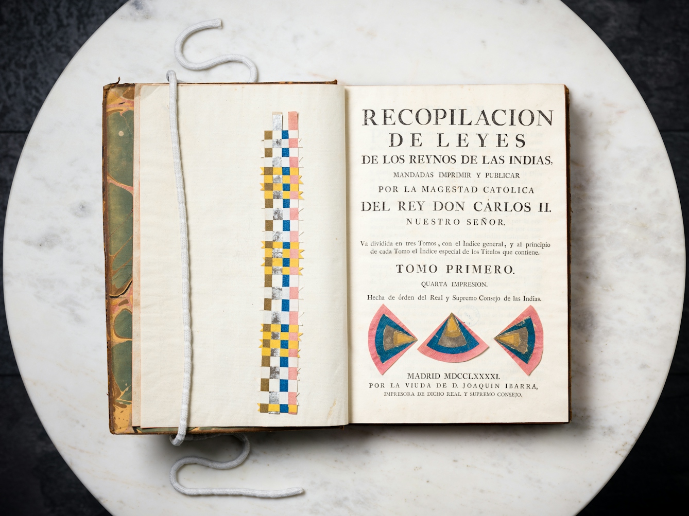 An old book propped open on a marble tabletop, with paper jewellery placed inside.