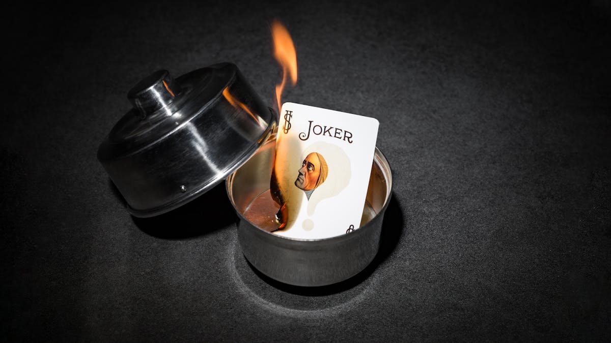 Photograph of a burning joker card in a silver dish. On the card is the face of the 1920s mind reader, Alexander.