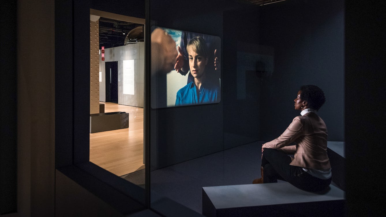 Photograph of a woman sitting watching a film projection in a dark gallery space.