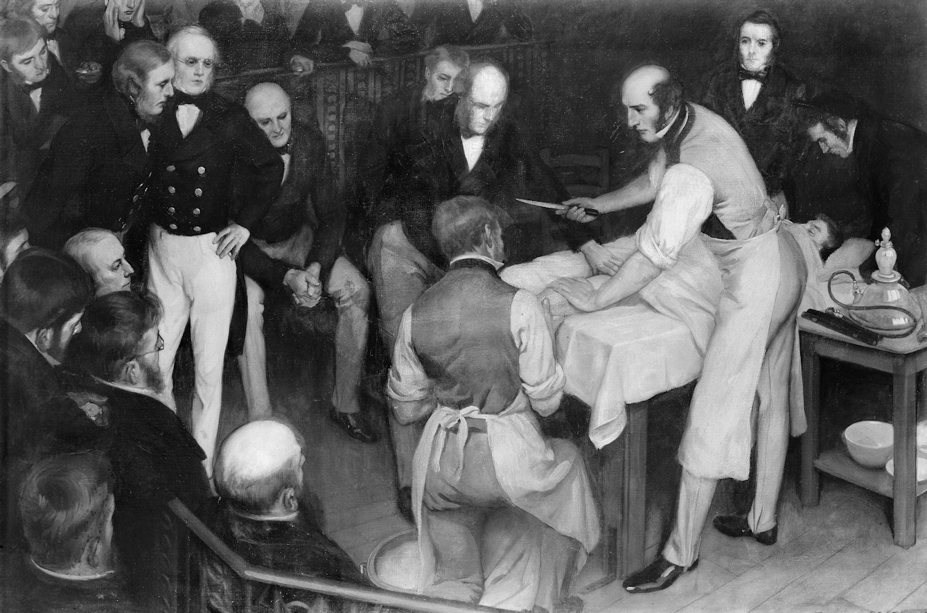 Black and white photograph of a painting depicting Robert Liston operating, surrounded by an audience of men in dark coats and white breeches. Liston has his white shirt-sleeves rolled up and is holding a knife and leaning over a body that is covered in a sheet. Liston and one other man facing away from the viewer wear aprons. 