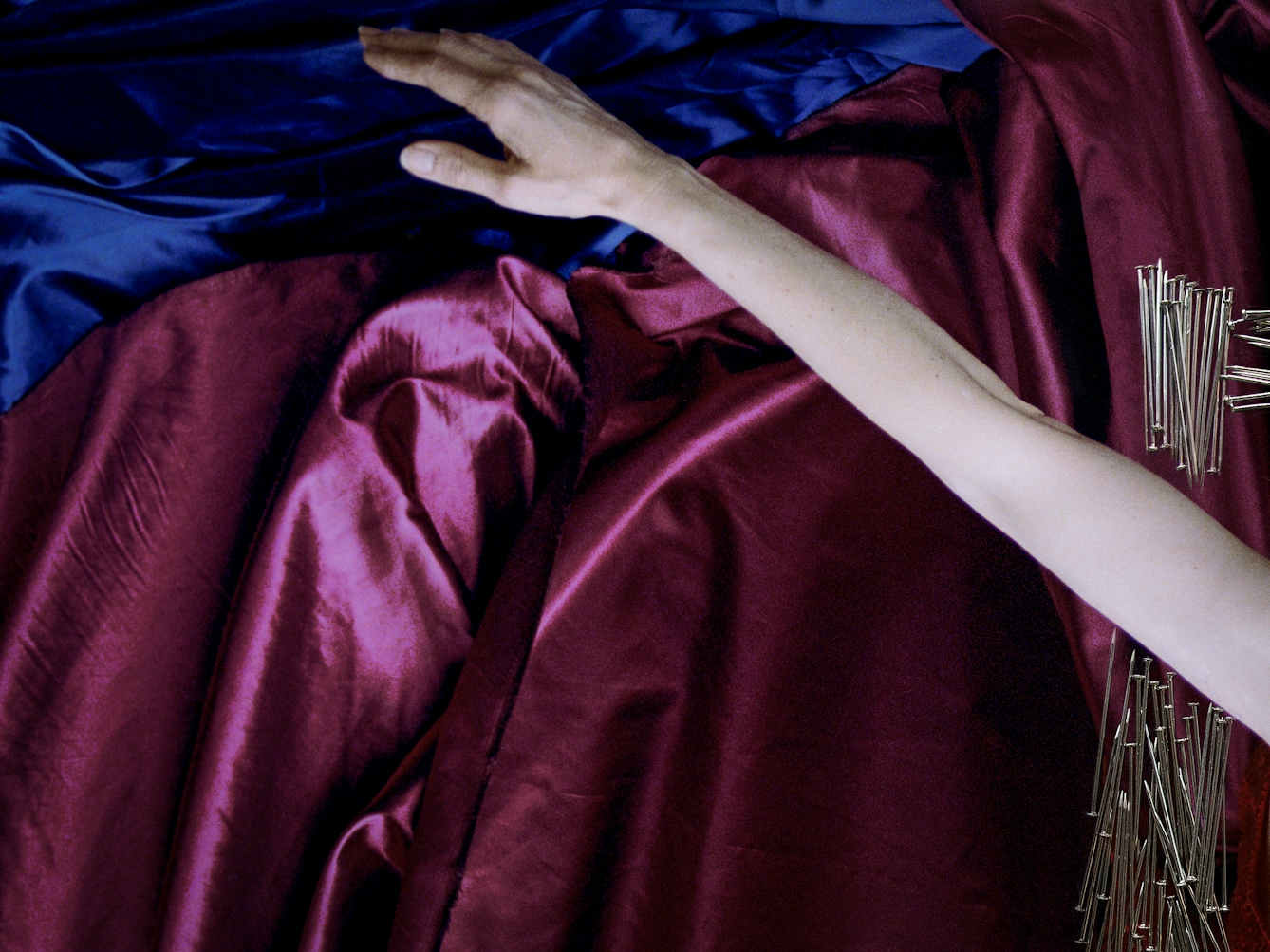 Detail from a larger artwork created with a colour photographic print of a female figure in a bright red dress, set against a purple and blue draped silk background. Her arm is extended out to the side, hand stretched out. Just visible is one side of the pin frame which stops above and below her extended arm making it look as if she is bursting through the frame.