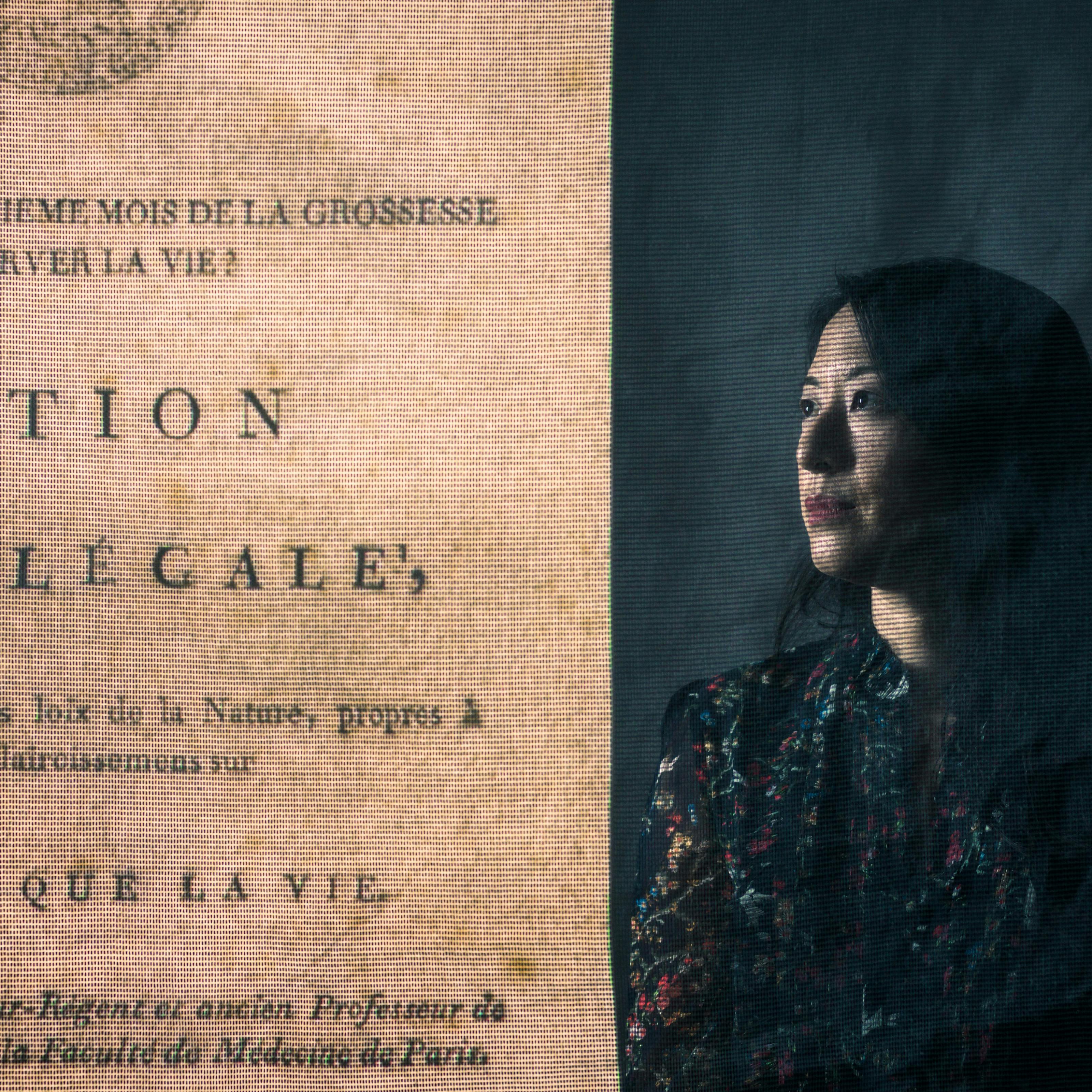 Photograph of a young woman standing behind a projected image of a page from an early printed book.