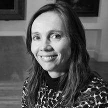 Black and white photograph of Julia Nurse, a white woman with brown hair, smiling. She wears an animal-print dress and the corners of paintings are visible in the background.