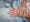 Photograph of the hands of a patient with bright turquoise painted fingernails, resting on a light blue hospital bedsheet.