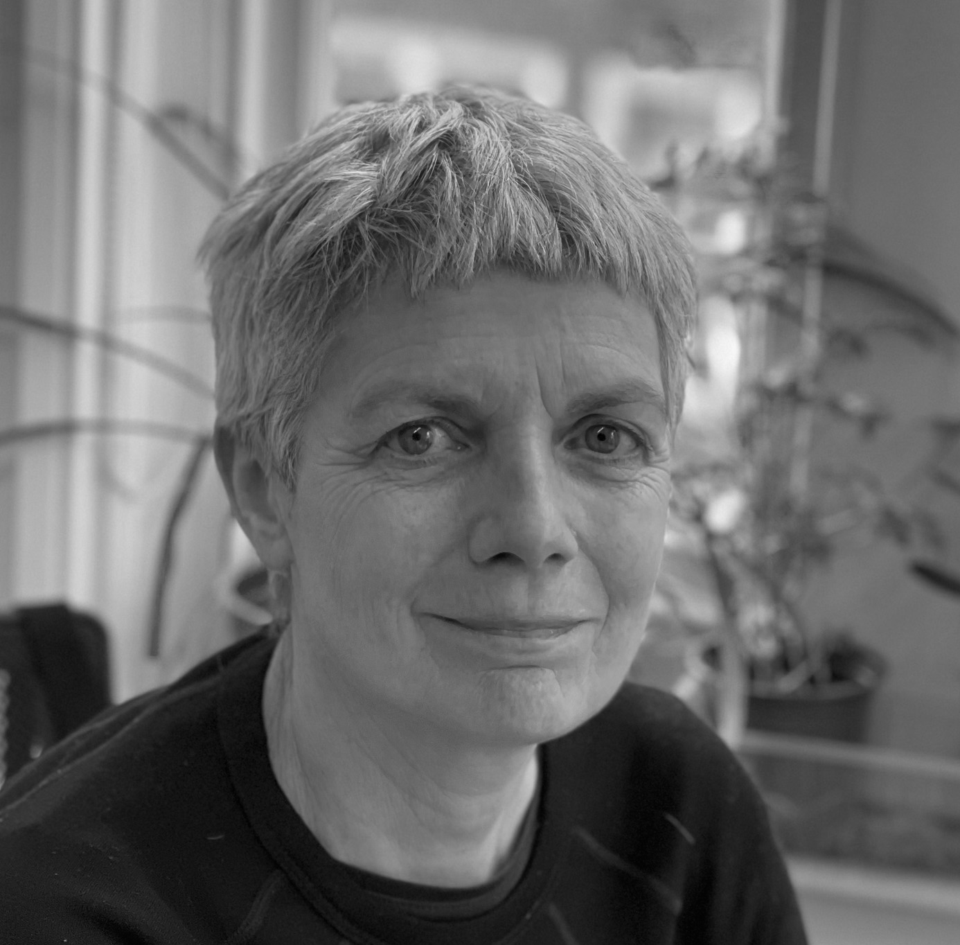 Black and white photograph of the head and shoulders of a middle-aged white woman with cropped blond hair. The woman is smiling and looking straight at the viewer.