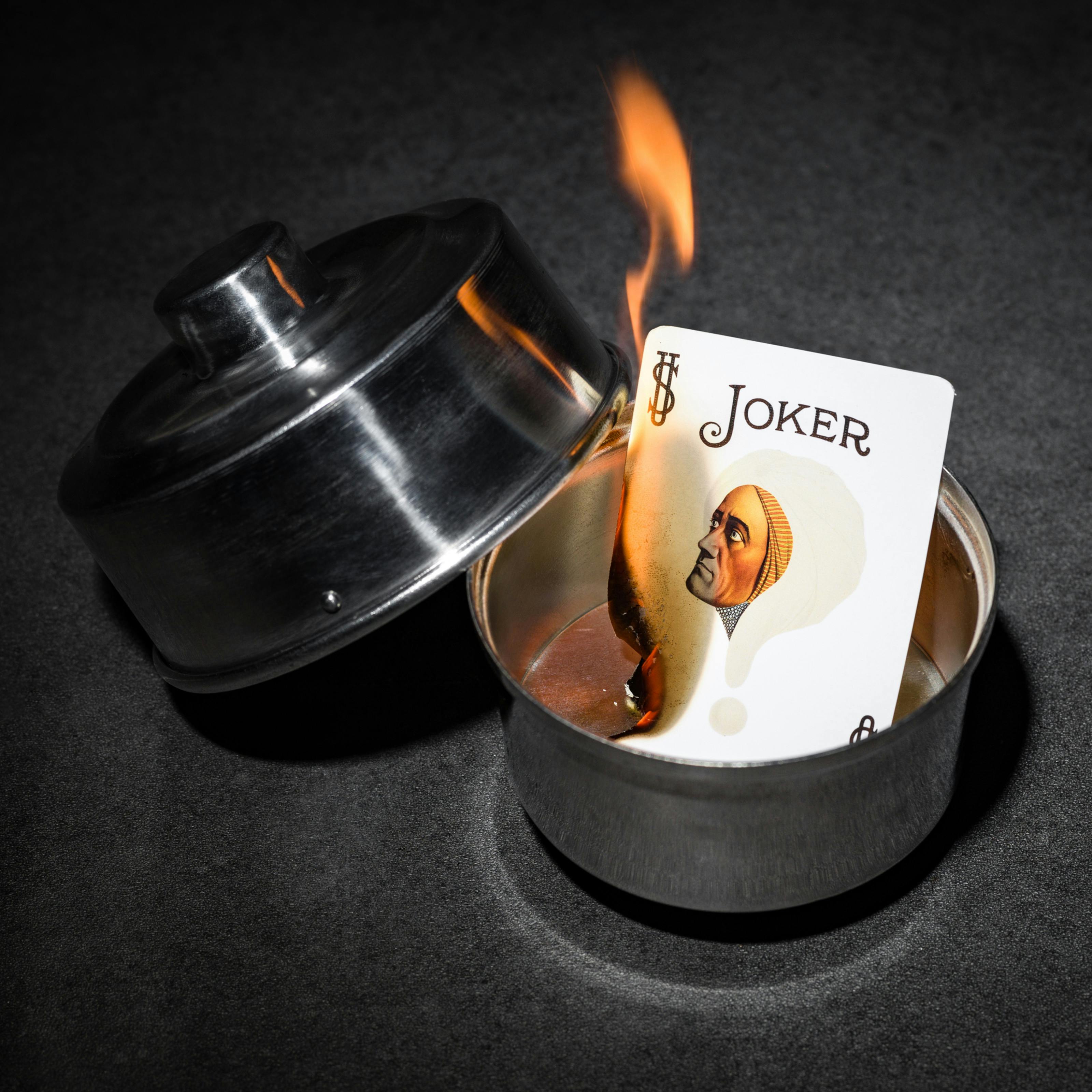 Photograph of a burning joker card in a silver dish. On the card is the face of the 1920s mind reader, Alexander.