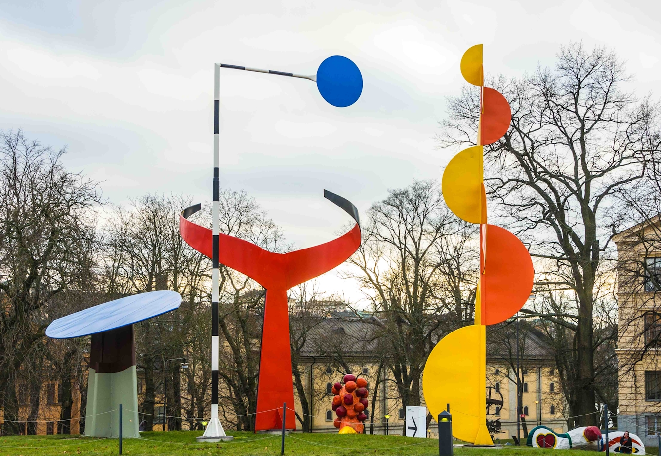 A large multipart open-air sculpture, featuring metal shapes includiding circles and semi-circles in orange, yellow, red and blue.
