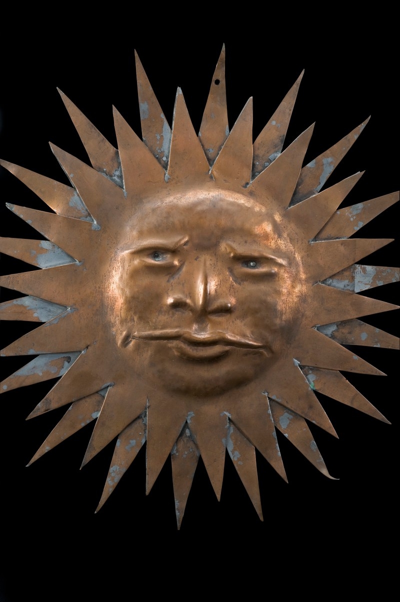 Image of copper Sun-shaped sign with a face
