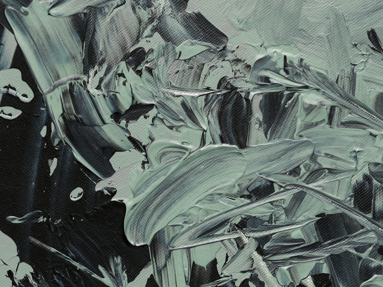 Photograph of close-up detail of a larger abstract expressionist painting on a large circular canvas, titled 'Binaries'. It is predominantly monochrome. The background layer is completely covered with grey and green-grey hues. Textural qualities have been captured in the acrylic paint including impressions made by deep brush strokes and gathered, layered paint. Black expressionist marks, created with a palette knife, scatter across the surface and begin to accumulate towards one side of the canvas. Some marks include waves of banded black and grey. The black marks are reminiscent of a murder of crows, with their onyx wings stretching and taking flight.