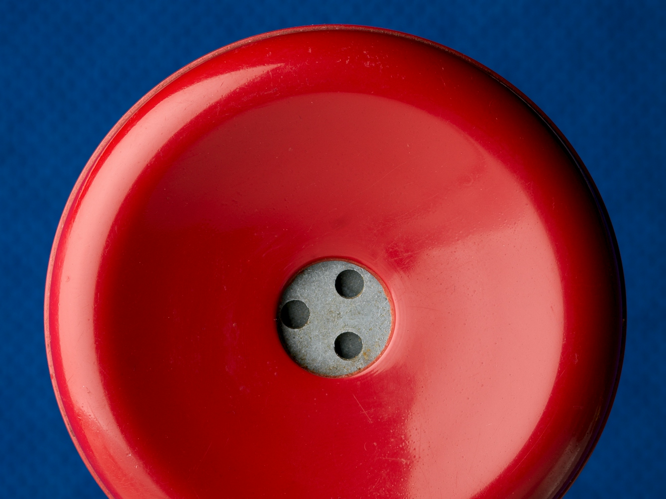 Photograph of a close up of an old red rotary telephone receiver's earpiece, against a blue felt background. 