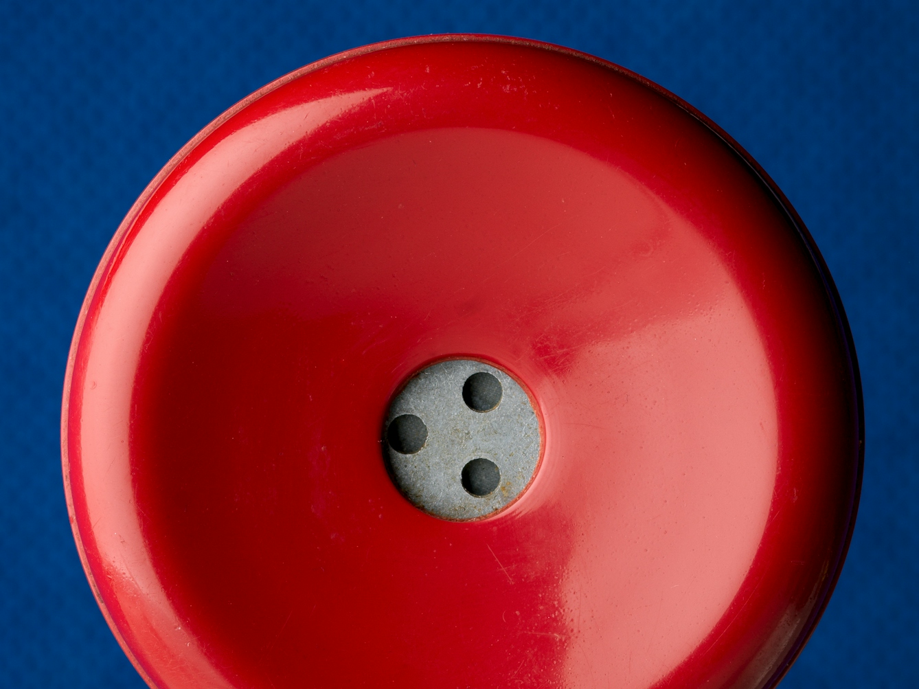 Photograph of a close up of an old red rotary telephone receiver's earpiece, against a blue felt background.