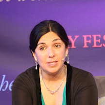 Photograph of Katharine Quarmby, who is sat in front of a purple background and speaking into a hands-free microphone. 