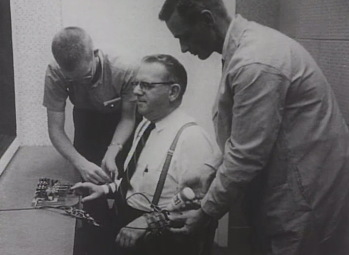 Two men attach wires to a subject in an experiment.