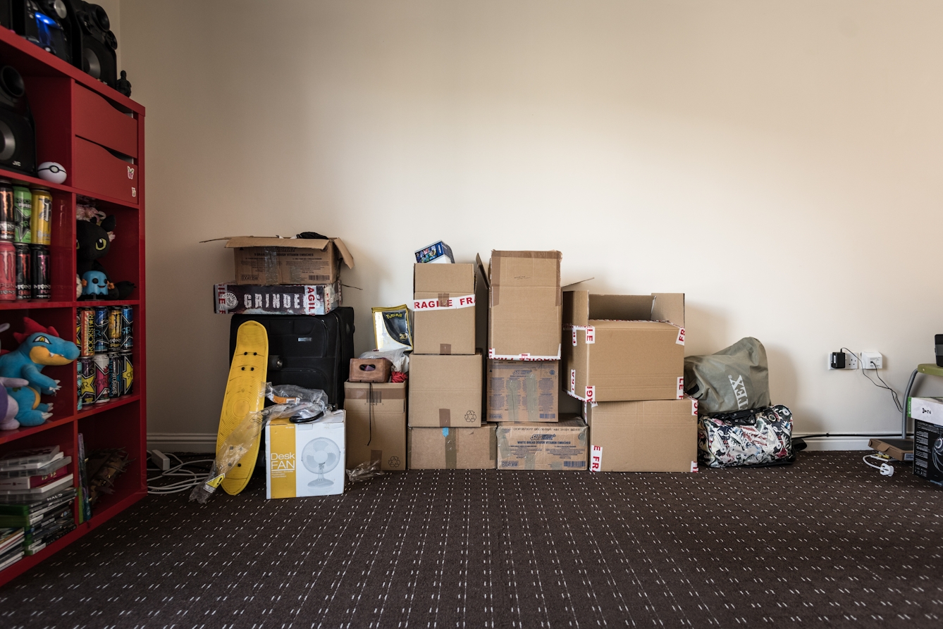 Photograph of unpacked boxes piled up against a wall inside a living room.
