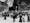 Black and white photograph of people kneeling at a shrine in Lourdes. Beside the worshippers, crutches can be seen hanging up.
