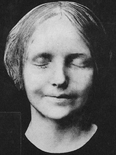 Black and white image of death mask of young woman. She has her eyes closed and has a faint smile.