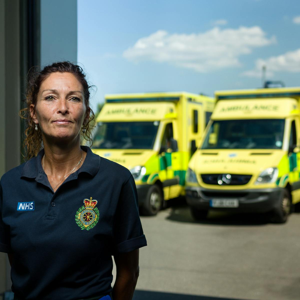 Photographic portrait of Mandy English, paramedic, at Hull East Ambulance Station, with ambulances in the background.