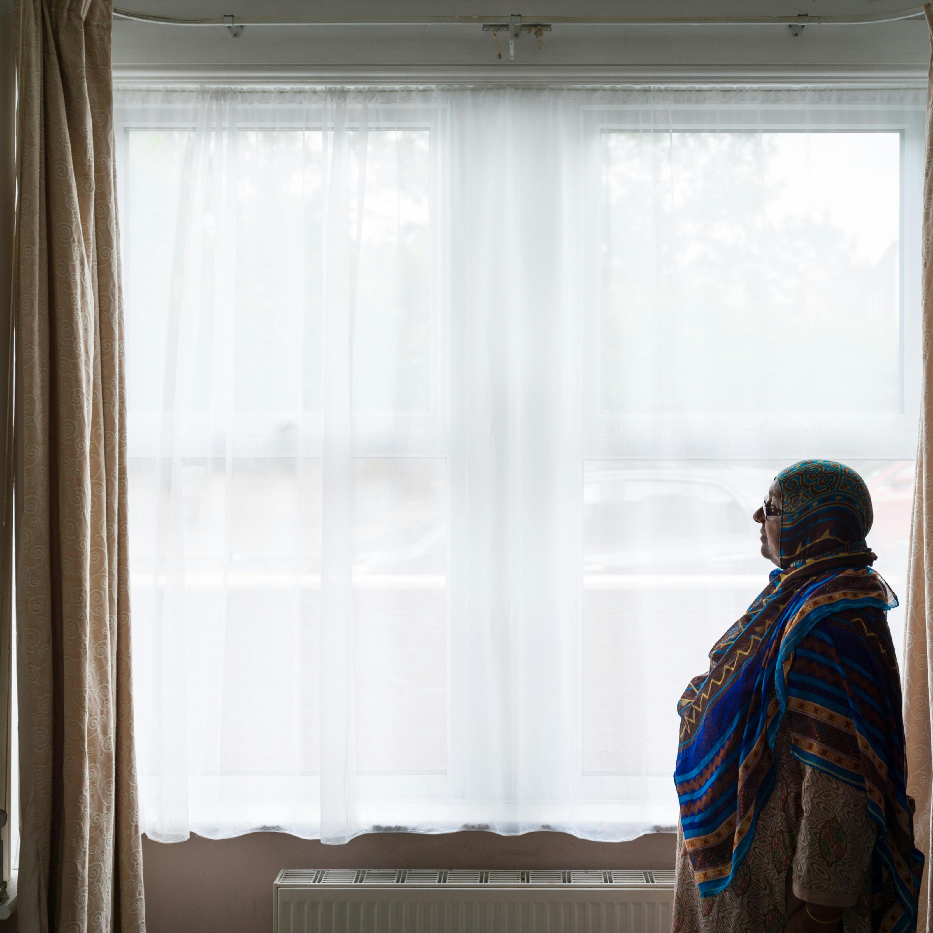 Photograph of a woman standing by the front windows in her living room.