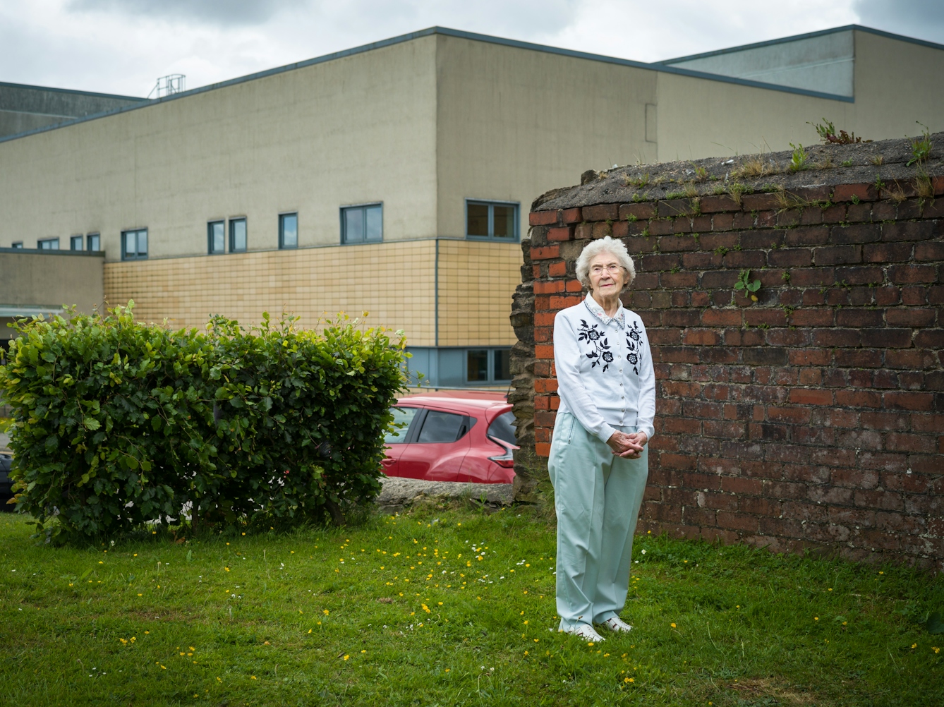 Photographic full length portrait of Joyce Thompson, retired nurse, outside the Royal Blackburn Hospital.