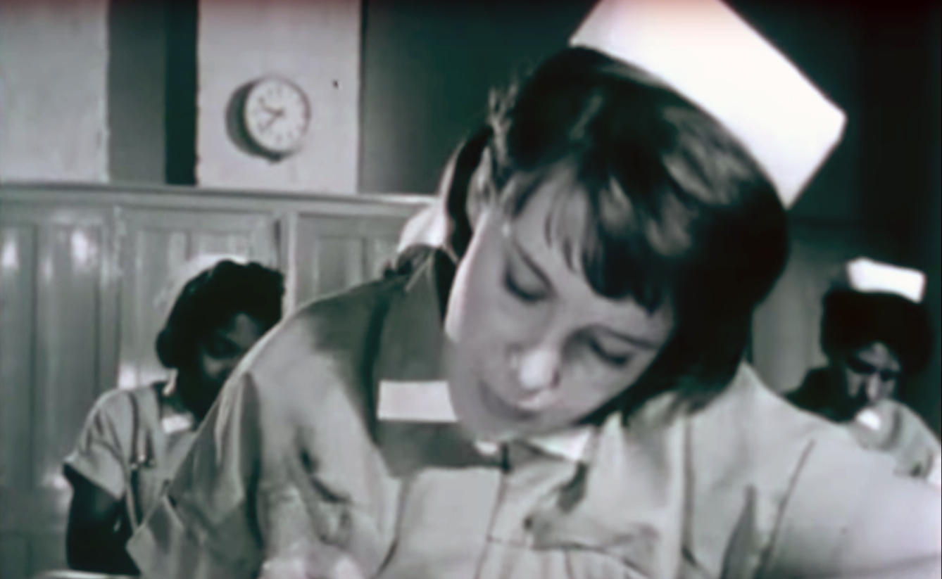 A picture of three nurses leaning forward in concentration over an exam. 