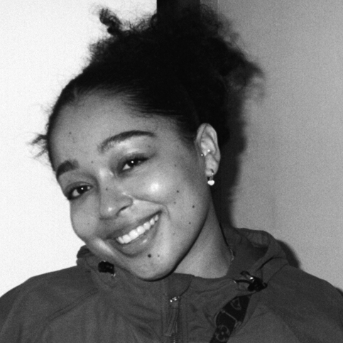 Head and shoulders photograph of a young woman, head tilted to one side, wearing an anorak zipped up to just below the chin.