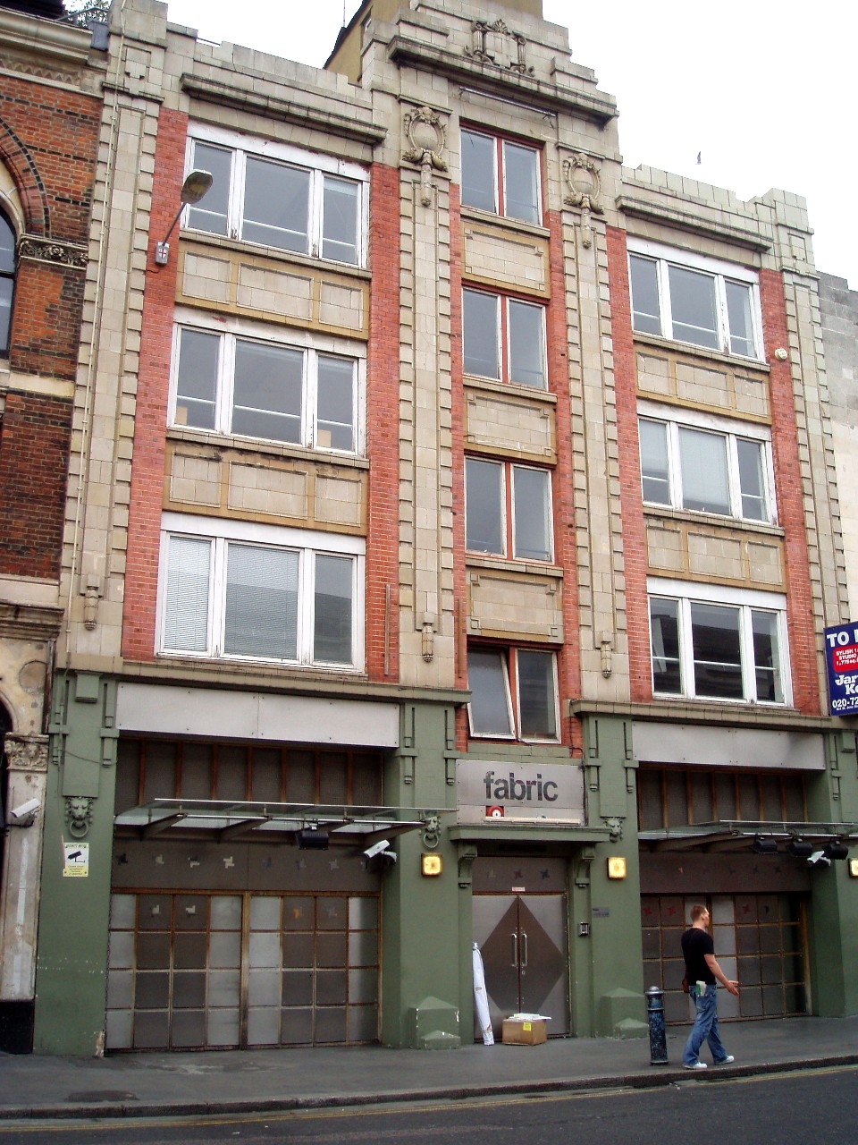 Colour photograph of the exterior of a three–storey red brick building with the entrance to a nightclub on street level.