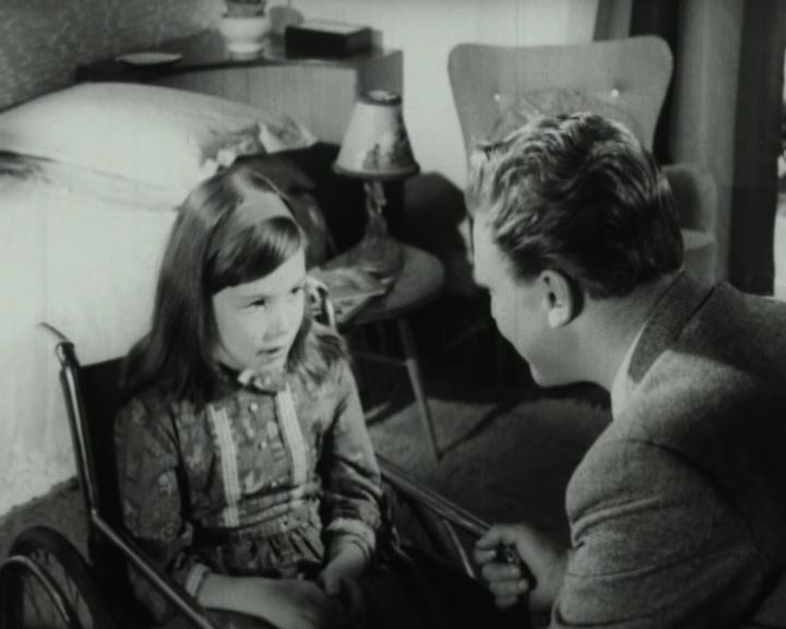 A girl in a wheelchair talks to a man with his back to the camera