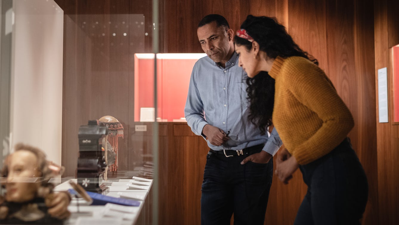 Two people standing in a gallery looking at material on display in a glass case, 