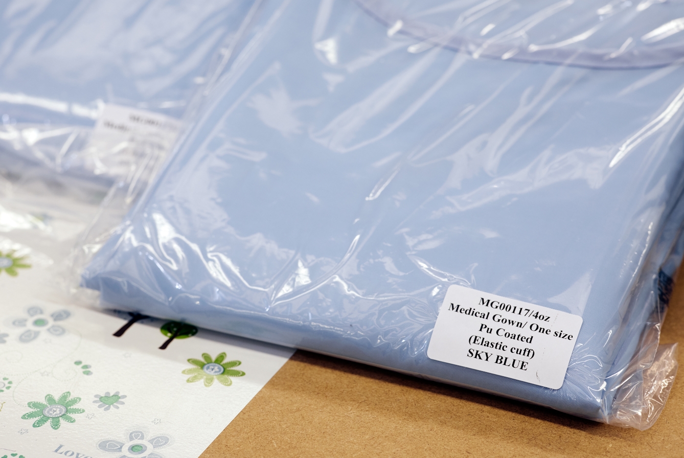 Photograph of a close up of a folded light blue medical gown packaged in a plastic wrapper.