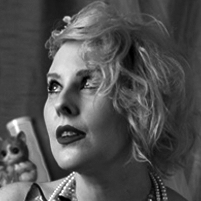 Photograph of the head of a woman with chin-length wavy hair, looking upwards and above.